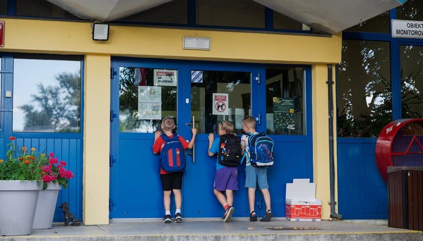 Trzech chłopców wchodzących do budynku szkoły.