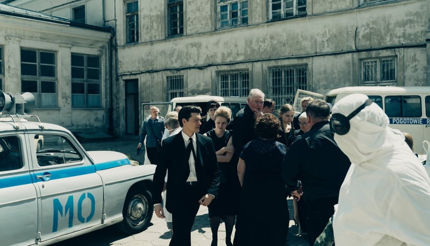 Kadr z serialu "Czarna śmierć". Na zdjęciu widać grupę osób ubranych na czarno oraz osobę w odzieży ochronnej i okularach