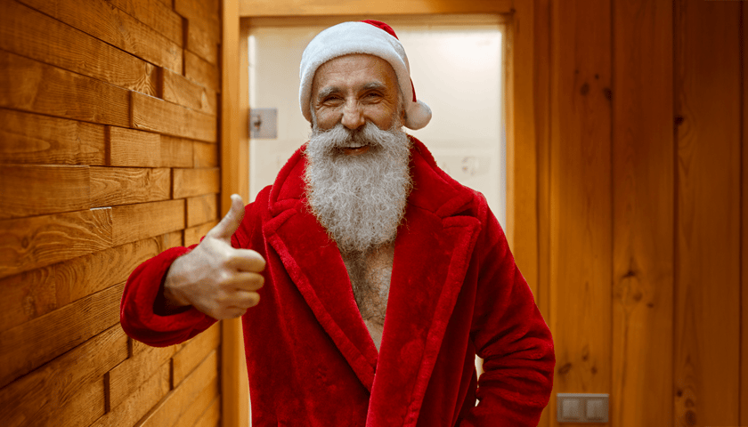 Mężczyzna w przebraniu mikołaja, w szlafroku czerwony, pokazuje kciuk w górę w drewnianym pomieszczeniu (zdjęcie ilustracyjne)