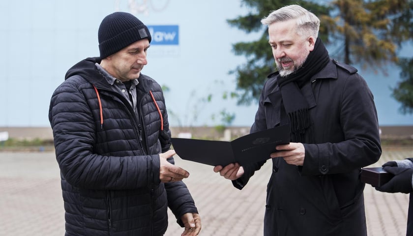 <p>Radosław Michalski, dyrektor Departaentu Marki Wrocławia wręcza Andrzejowi Tylkowskiemu odznakę i list gratulacyjny prezydenta Jacka Sutryka</p>