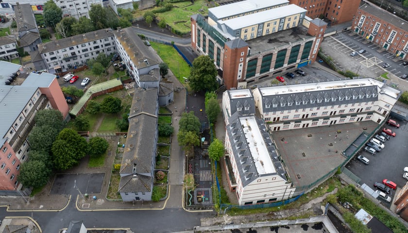 Na zdjęciu widoczne z góry, z lotu ptaka budynki, ulica, chodniki, trawniki i zaparkowane samochody./ The photo shows buildings, a street, sidewalks, lawns and parked cars visible from above.