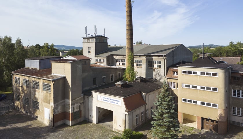 Na zdjęciu widoczne są budynki fabryczne, komin oraz niebo z chmurami./ The photo shows factory buildings, a chimney and a sky with clouds.
