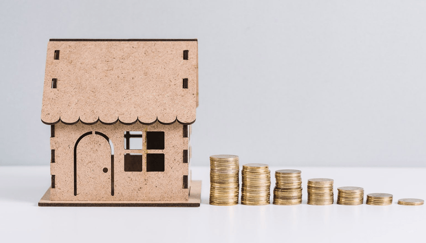 Zdjęcie ilustracyjne przedstawia makietę domu i stosy monet