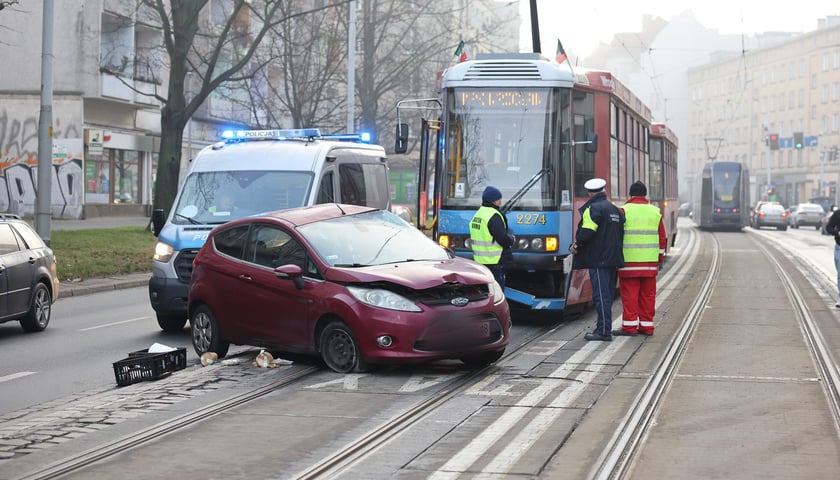 Wypadek - rozbity samochód na torach tramwajowych, za nim tramwaj, z przodu pracownicy służb