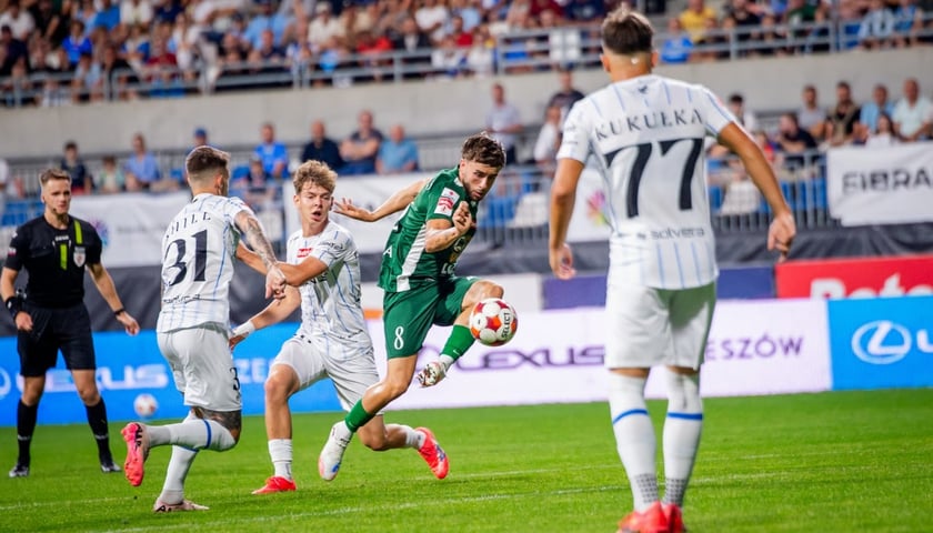 Sędzia i piłkarze na boisku w trakcie walki o piłkę.