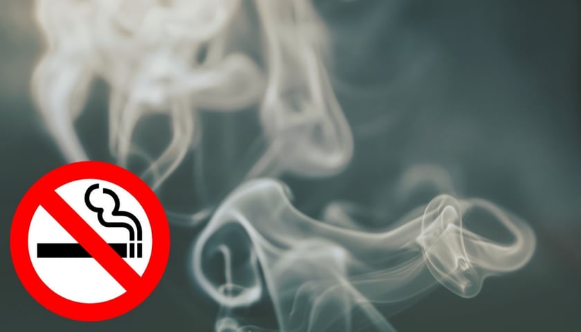 W tle dym papierosowy, u dołu po lewej stronie czerwone kółko z przekreślonym papierosem