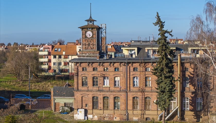 Widok na ceglany budynek z wieżą zegarową na terenie dawnej cukrowni na Klecinie (ul. Supińskiego)