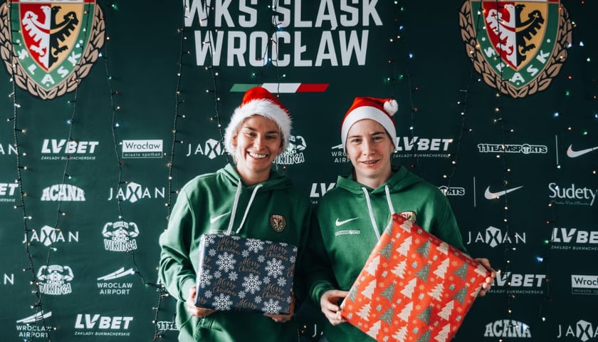 Dwie piłkarki Śląska Wrocław ubrane w mikołajowe czapki stoją z zapakowanymi prezentami.