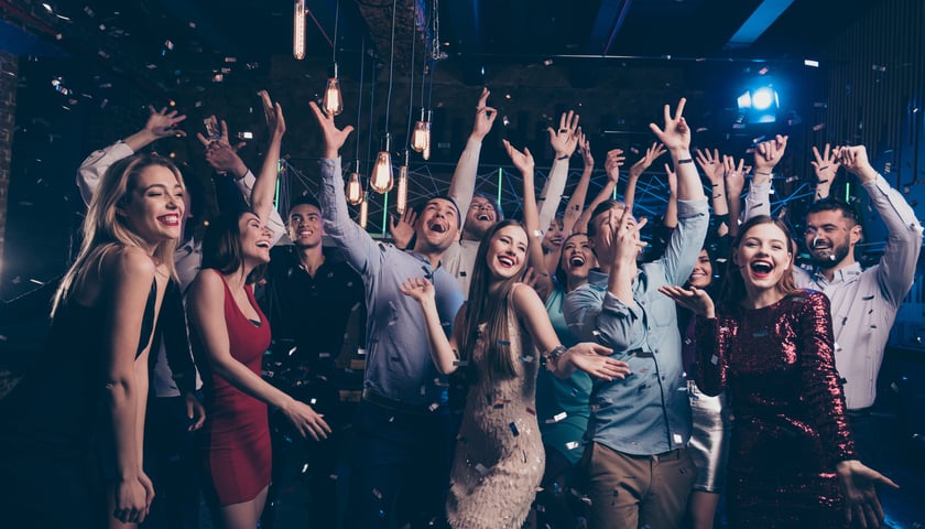 Rozbawione towarzystwo: kobiety i mężczyźni z podniesionymi rękami tańczą podczas balu sylwestrowego
