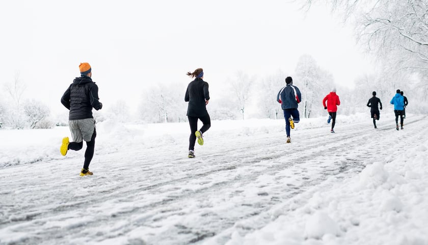 Grupa osób w sportowych ubraniach podczas biegu w terenie w okresie zimowym.