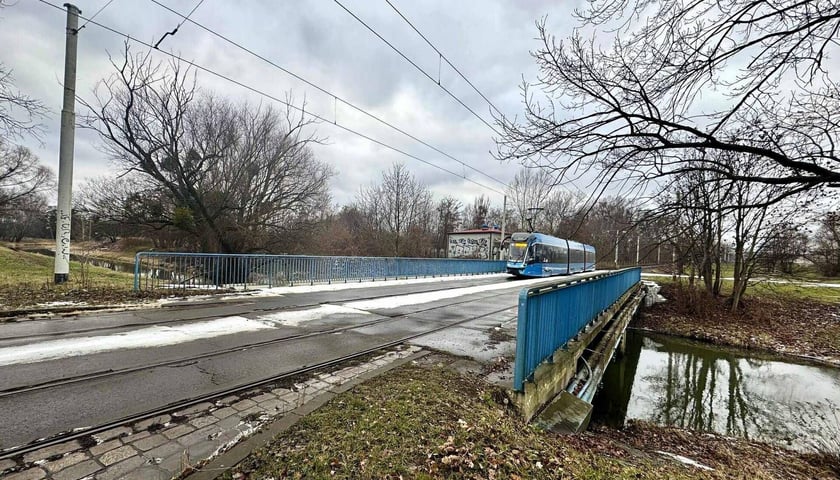 Widok na torowisko i most przez rzekę i jadący tramwaj. Obok Starego Mostu Pilczyckiego, który będzie remontowany, zostanie zbudowana kładka pieszo-rowerowa nad Ślęzą.