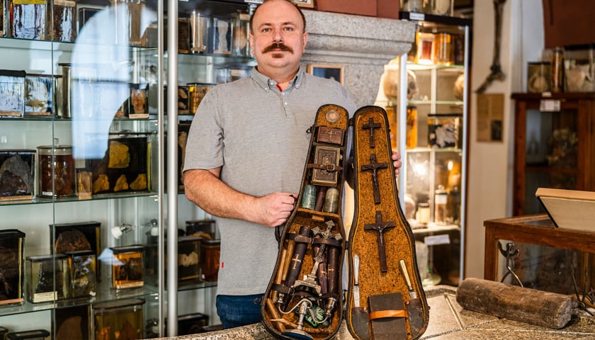 Dr Jędrzej Siuta z Zakładu Medycyny Sądowej UMW, opiekun Muzeum Medycyny Sądowej, prezentuje futerał z zestawem antywampirycznym. Na zdjęciu mężczyzna trzyma futerał, w którym znajdują się m.in. krucyfiksy, szklane butelki.