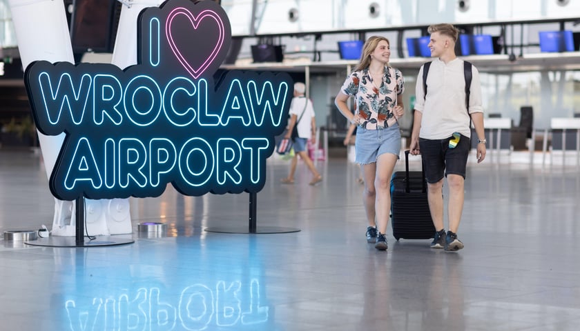 Dwoje ludzi w terminalu WPL, obok neonu I love Wroclaw Airport