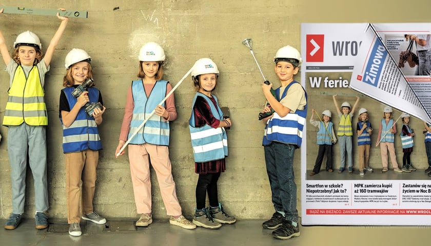 Sześcioro dzieci w kamizelkach odblaskowych i kaskach z metrówką, poziomnicą i innymi przyrządami budowlanymi na tle szatej ściany