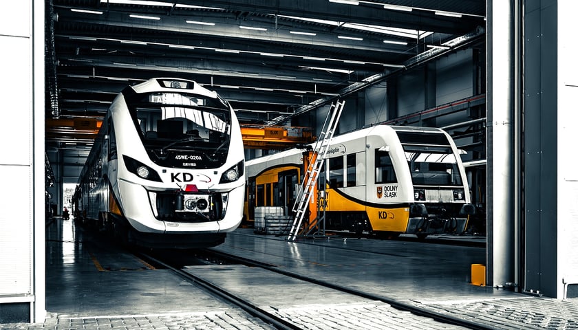 Dwa pociągi stojące w hangarze - składy Kolei Dolnośląskich w hali serwisowej.