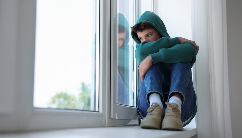 Na zdjęciu smutny chłopak siedzi patrzy przez okno. Zdjęcie ilustracyjne
