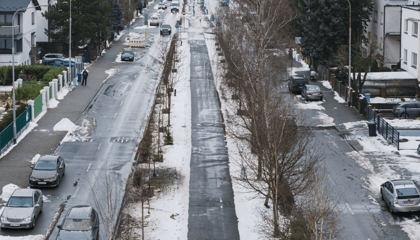 Widok z lotu ptaka na ścieżkę rowerową między zaśnieżonymi psami zieleni przy Alei Piastów na Oporowie.