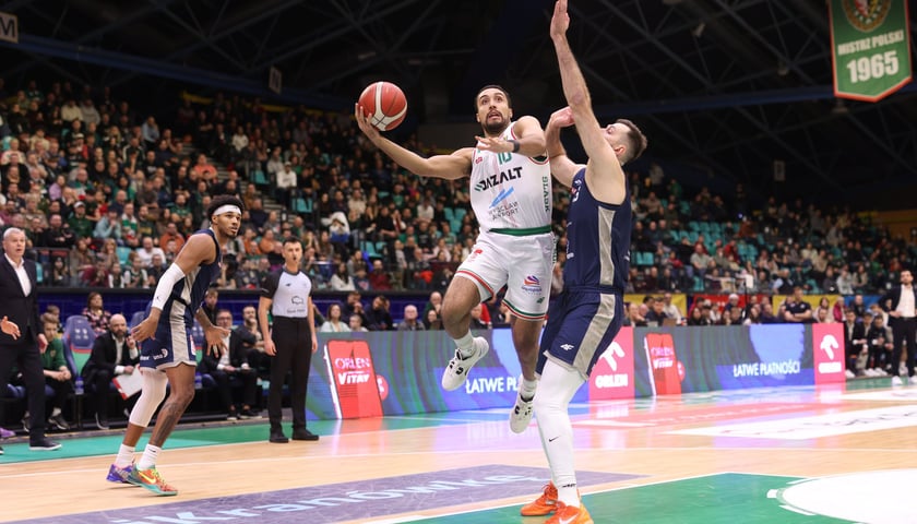 Koszykarz w wyskoku z piłką blokowany przez zawodnika przeciwnej drużyny - mecz Śląsk Wrocław - Dziki Warszawa (23 grudnia 2025 r. w hali Orbita). 