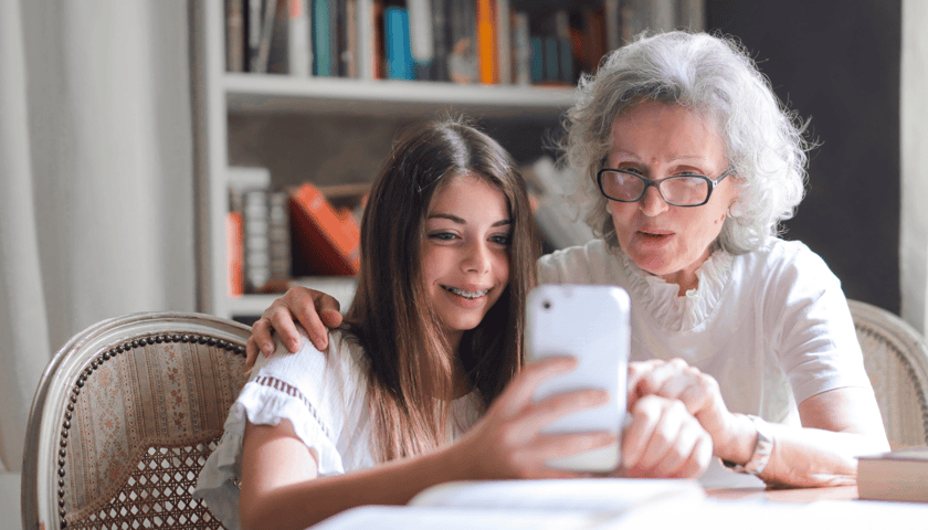 Zdjęcie ilustracyjne: 2 osoby, młoda dziewczyna oraz seniorka, oglądają coś na ekranie smartfona