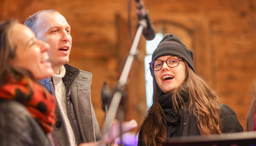 Wspólne kolędowanie w dawnym kościólku św. Jana Nepomucena, stojącym w Parku Szczytnickim. Wrocław, 24.01.2026. Na zdjęciu dwie kobiety i mężczyzna przy mirkofonie.