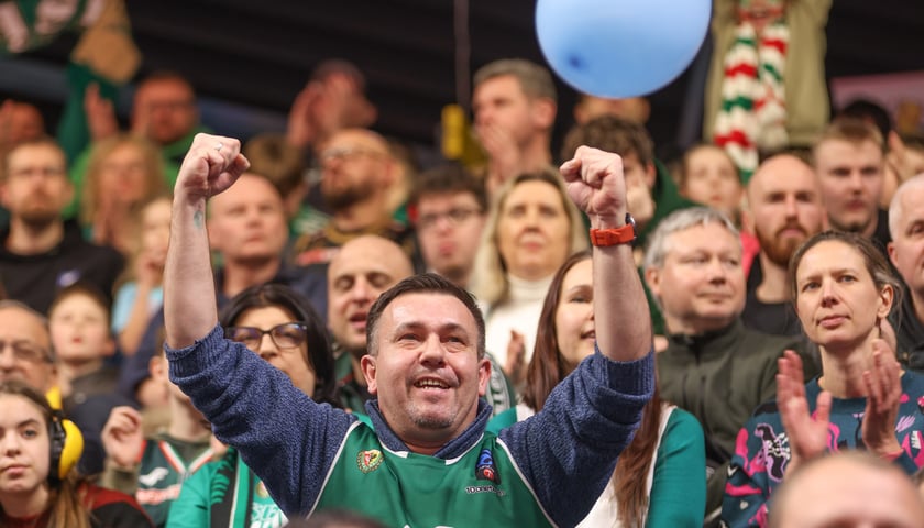 Mężczyzna wznoszący ręce do góry i inni kibice na trybunie Hali Orbita podczas meczu z Treflem Sopot