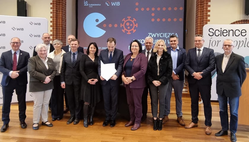 Kobiety i mężczyźni stoją pod banerem promującym projekt PACMAN