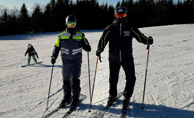 Policyjny patrol narciarski w kompleksie Górnik w Rzeczce. Na zdjęciu dwie osoby w kombinezonach narciarskich z oznaczeniami policyjnymi, kaskach i na nartach