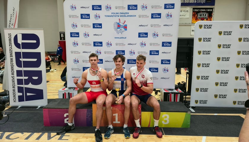 Medaliści XXXV ENEA Mistrzostw Polski na ergometrze wioślarskim. Pierwszy z lewej: Michał Rańda. Na zdjęciu trzej młodzi mężczyźni w strojach sportowych prezentują medale po dekoracji