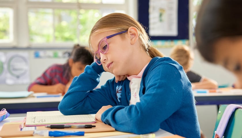 Na zdjęciu zmęczona dziewczynka w szkolnej ławce. Zdjęcie ilustracyjne