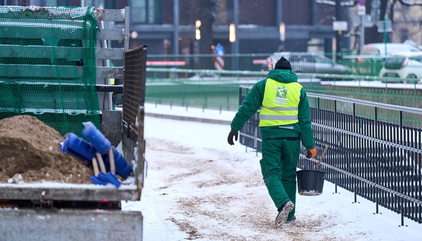 Członek ekipy wykonawcy Ekosystemu posypuje ośnieżone chodniki piaskiem - 17 lutego