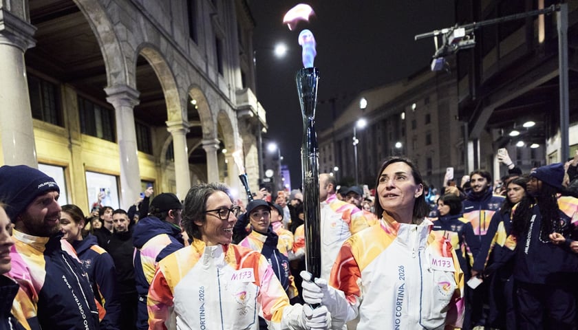Dwie osoby niosące znicz olimpijski na ulicy w Mediolanie