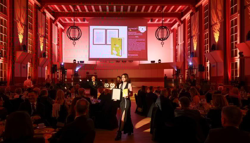 Licytacja podczas balu - ludzie siedzą na krzesłach w obszernej auli, trwa aukcja