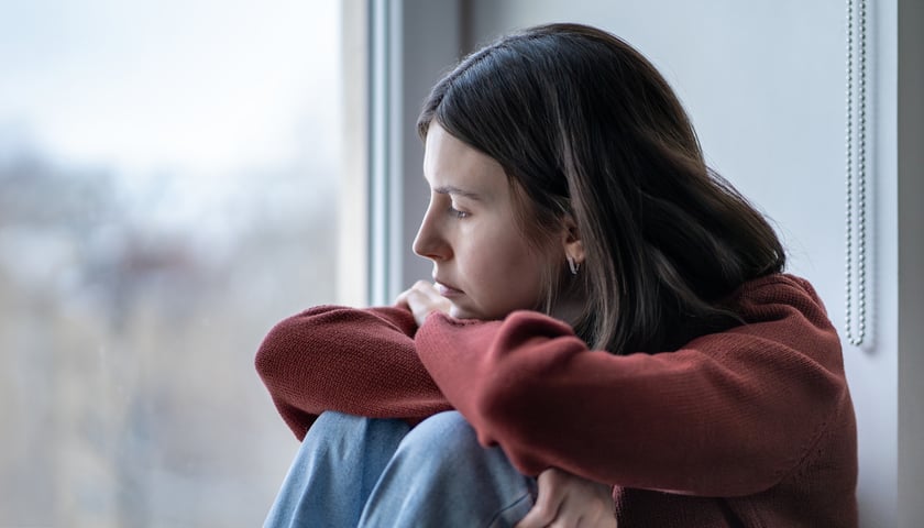 Na zdjęciu smutna dziewczyna siedzi i patrzy przez okno. Zdjęcie ilustracyjne