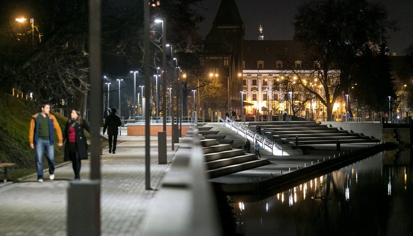 <p>Widok wieczorny na Bulwar Dunikowskiego wzdłuż Odry z zabudowaniami na Wyspie Piasek w tle.</p>