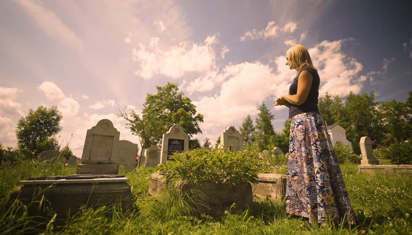 Kadr z filmu „Opiekunowie (nie)pamięci” . Na zdjęciu młoda kobieta stoi przy nagrobku