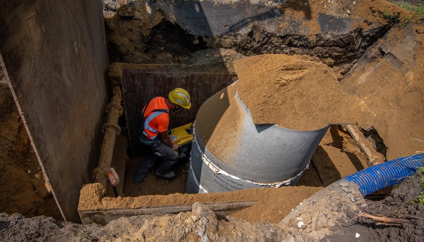 Mężczyzna w stroju roboczym montuje rurę w ziemi