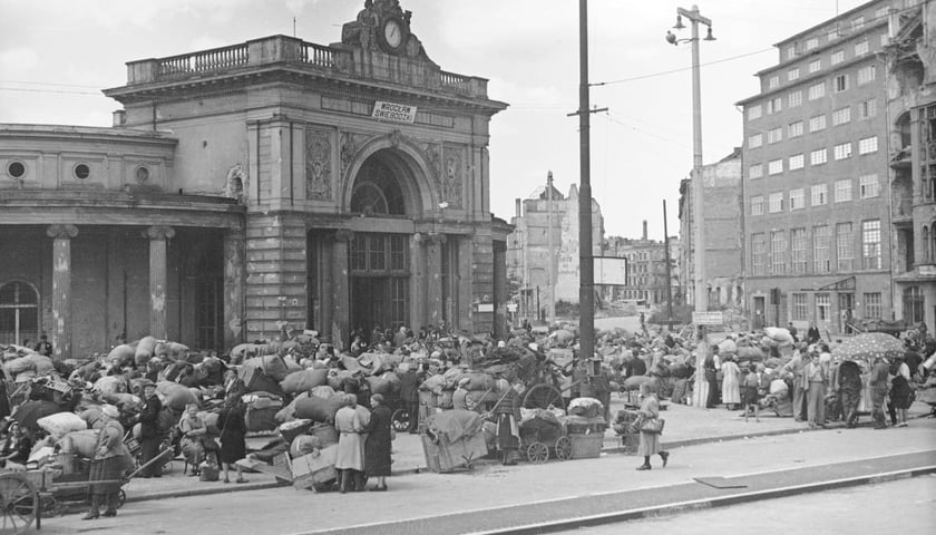 Okolice Dworca Świebodzkiego we Wrocławiu tuż po II wojnie. Na zdjęciu zabytkowy budynek oraz tłum ludzi z wózkami wypełnionymi pakunkami 