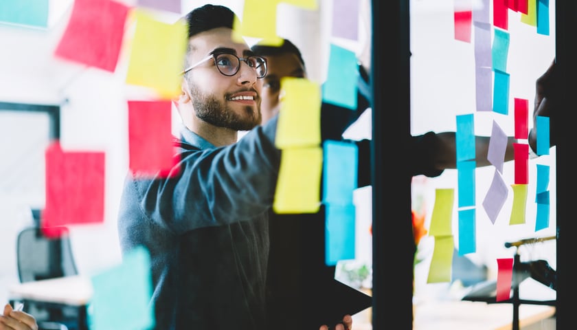 Mężczyzna stoi przed tablicą z poprzyklejanymi kolorowymi karteczkami