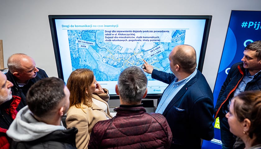 Spotkanie z mieszkańcami na Kłokoczycach ws. kanalizacji w roku 2024; kilka osób patrzy na ekran, na którym widać drogi komunikacji na czas inwestycji - zdjęcie ilustracyjne.