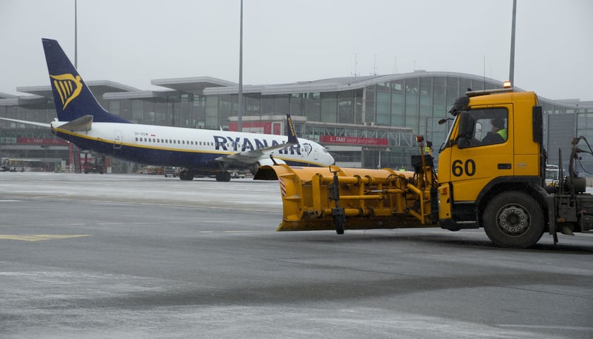 Sprzęt odśnieżający na płycie wrocławskiego lotniska. W tle terminal i samolot linii Ryanair.