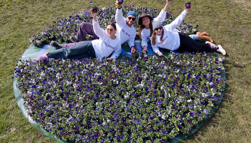Ludzie leżą na trawie wśród kwiatów w doniczkach