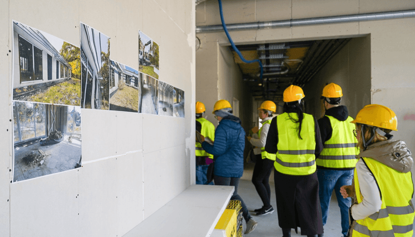 Dzień otwarty Publicznego Przedszkola Dębinka na Sołtysowicach. Na zdjęciu grupa osób w kaskach i kamizelkach zwiedza plac budowy