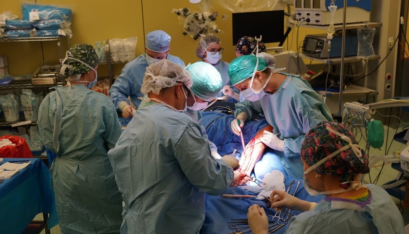 Operacja w Klinice Chirurgii Szczękowo-Twarzowej USK Wrocław. Na zdjęciu sala operacyjna podczas zabiegu, wokół stołu operacyjnego stoją osoby w fartuchach lekarskich