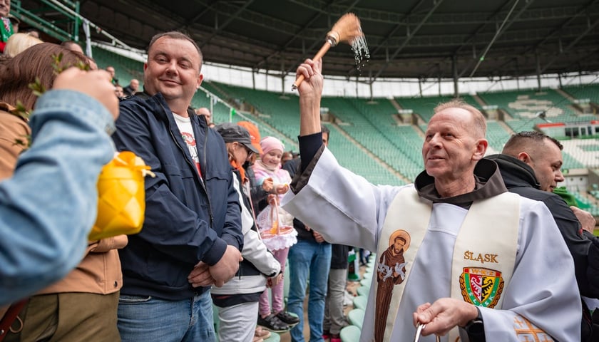 Święcenie pokarmów na Tarczyński Arena Wrocław. Na zdjęciu duchowny w komży i z kropidłem święci pokarmy w koszyczkach
