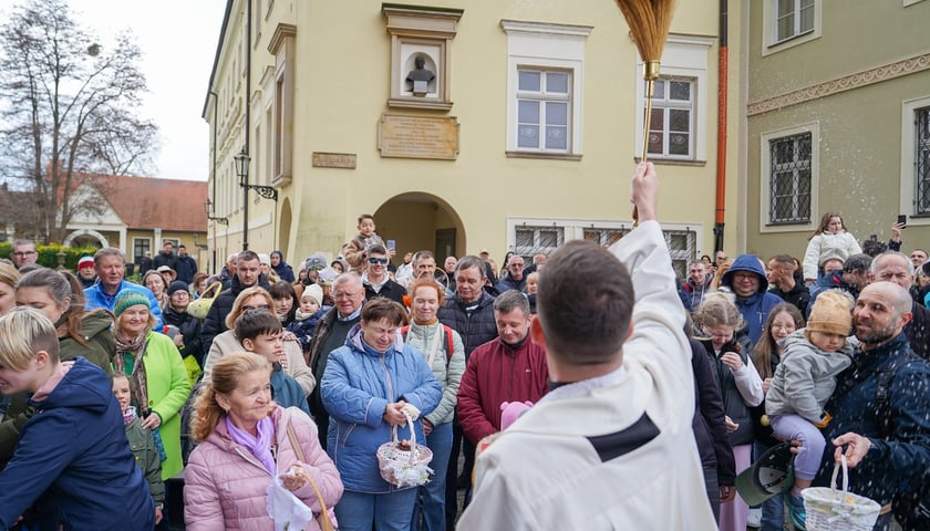 Święcenie pokarmów przed katedrą na Ostrowie Tumskim. Na zdjęciu ksiądz z kropidłem i ludzie z koszyczkami ze święconką
