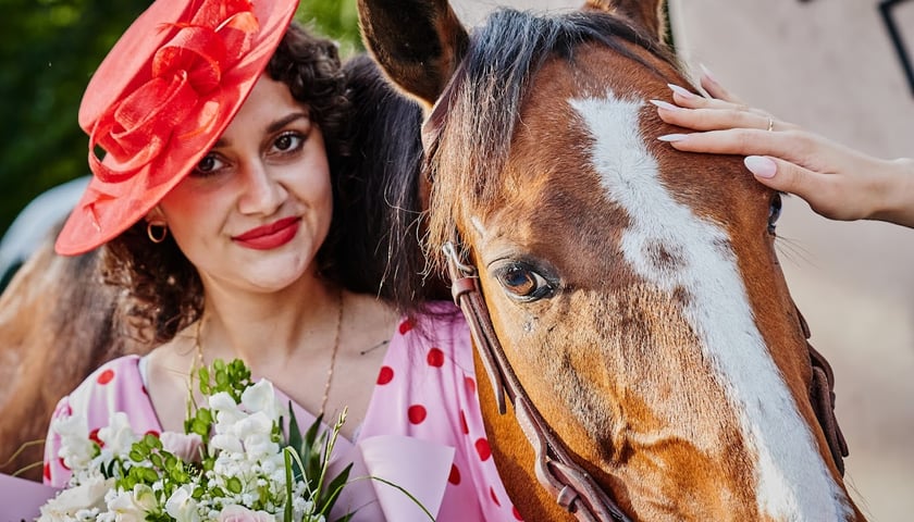 Wrocławski Tor Wyścigów Konnych. Na zdjęciu kobieta w sukience i kapeluszu przytula głowę konia