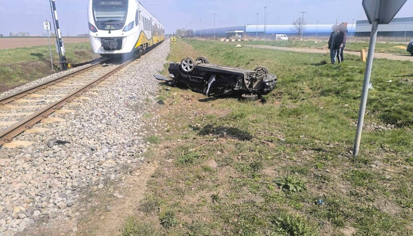 Zdjęcie przedstawiające rozbite auto leżące na dachu przy torach kolejowych i pociąg w tle - wypadek na przejeździe w Chrzanowie 11 kwietnia 2026 r.