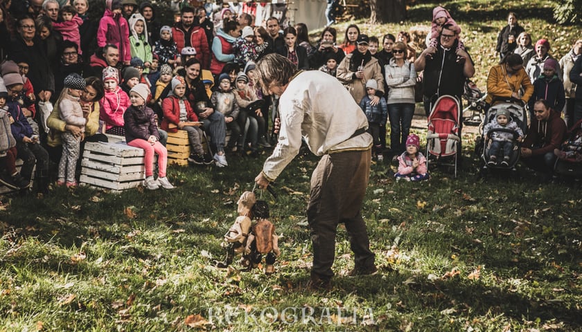 Powiększ obraz: Na zdjęciu tłum dzieci przygląda się kuglarzowi z marionetkami występującemu na trawie