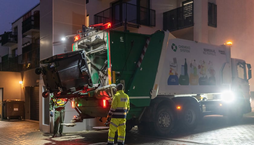 Powiększ obraz: Na zdjęciu śmieciarka odbierająca kontener z odpadami