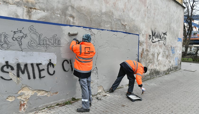 Powiększ obraz: Na zdjęciu dwóch mężczyzn skazanych za przestępstwa zamalowuje napisy mowy nienawiści na jednym z budynków we Wrocławiu